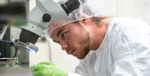 a research student in personal protective equipment using a microscope